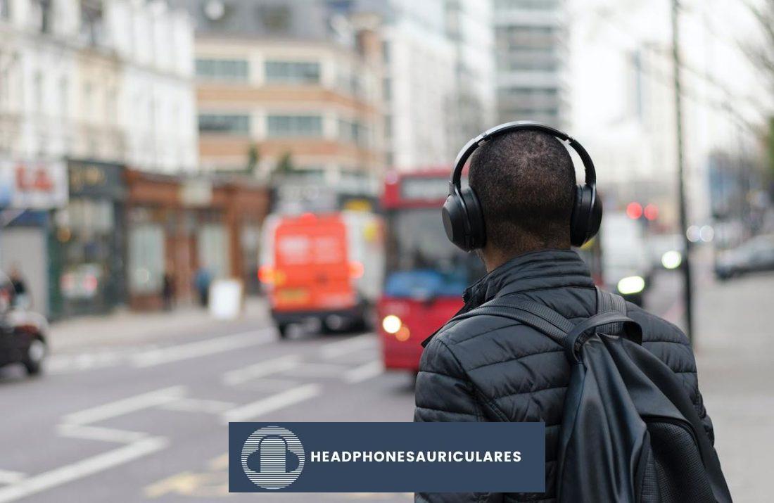 Hombre con audífonos en la acera de una ciudad (De: Unsplash).
